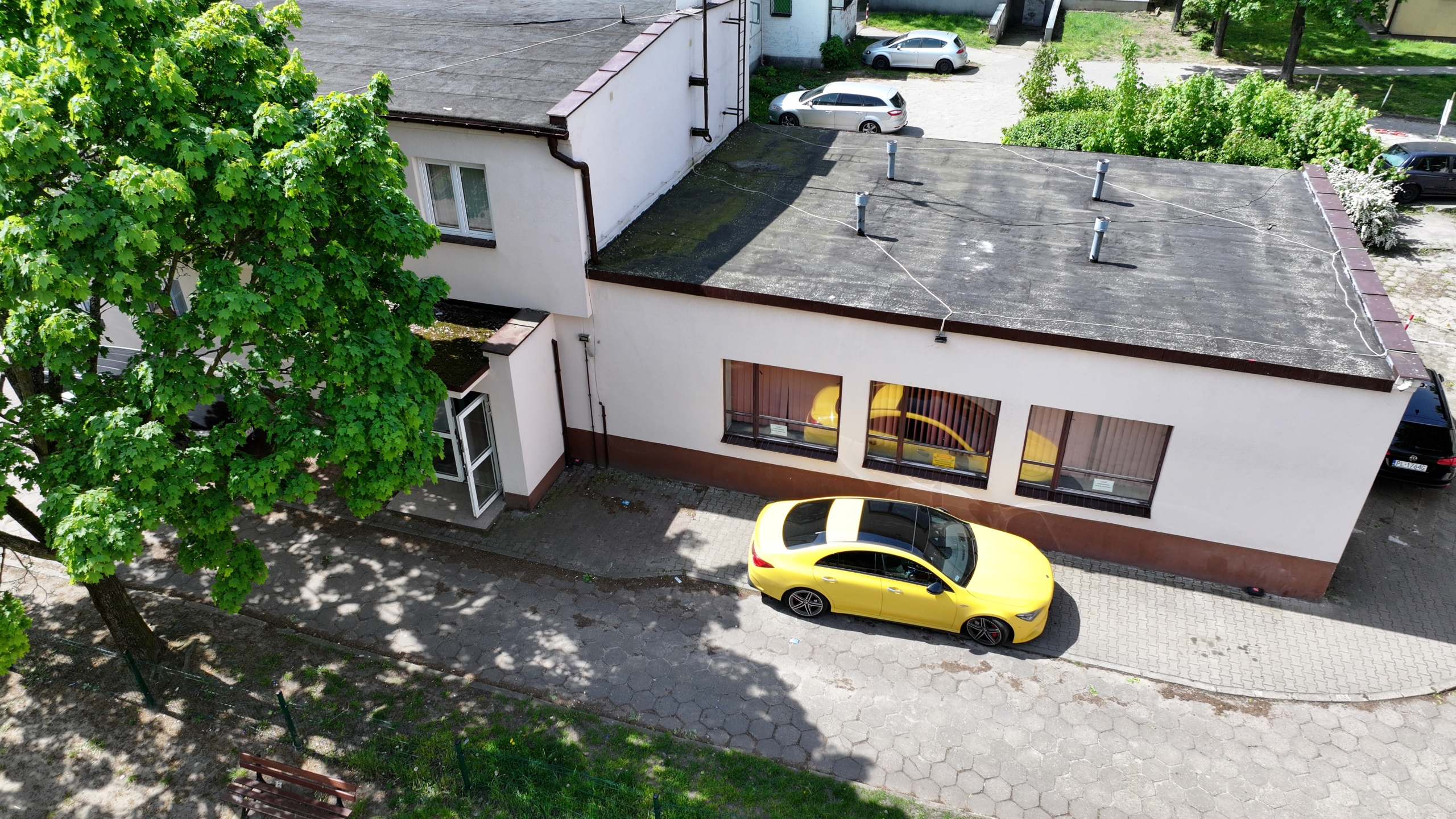 Widok z lotu ptaka na budynek w którym znajduje się lokal użytkowy w Lesznie i zaparkowany samochód na miejscu postojowym.